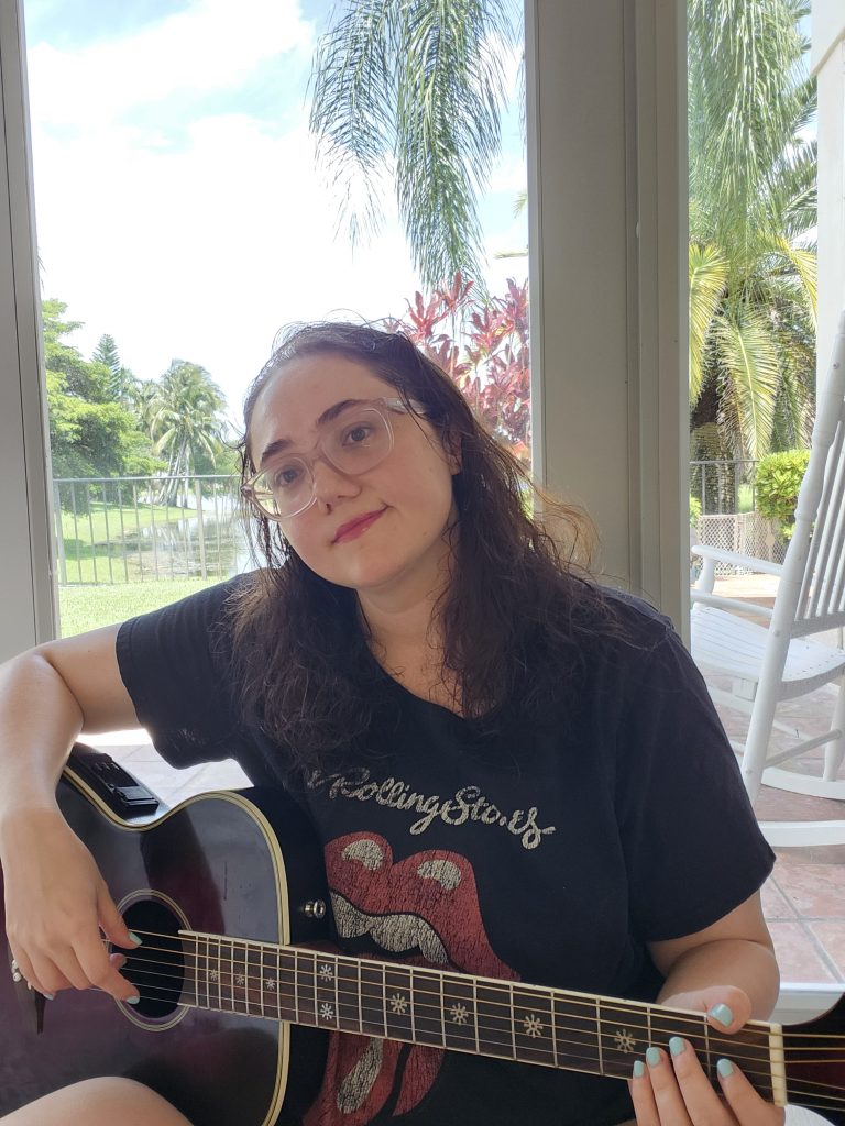 Lauren Grace Zemel with acoustic guitar, Rolling Stones shirt, natural light, South Florida background