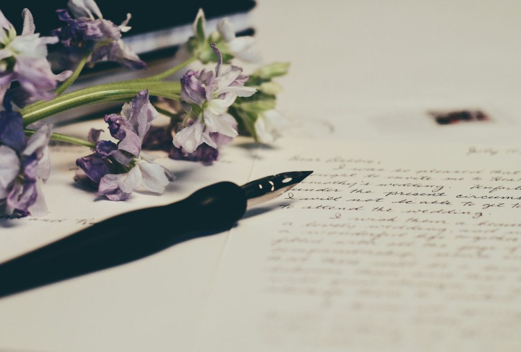 A fountain pen resting on a handwritten letter surrounded by dried purple flowers, representing the Poetry category