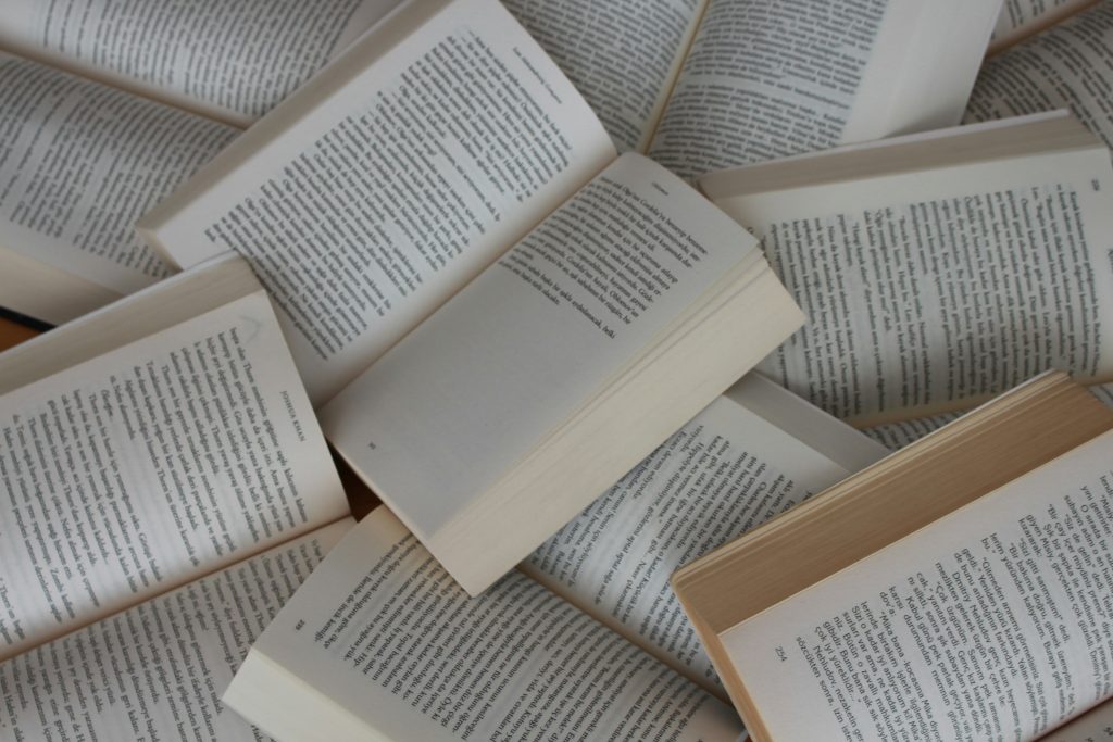 A scattered pile of open books with visible text pages, representing the Novels category