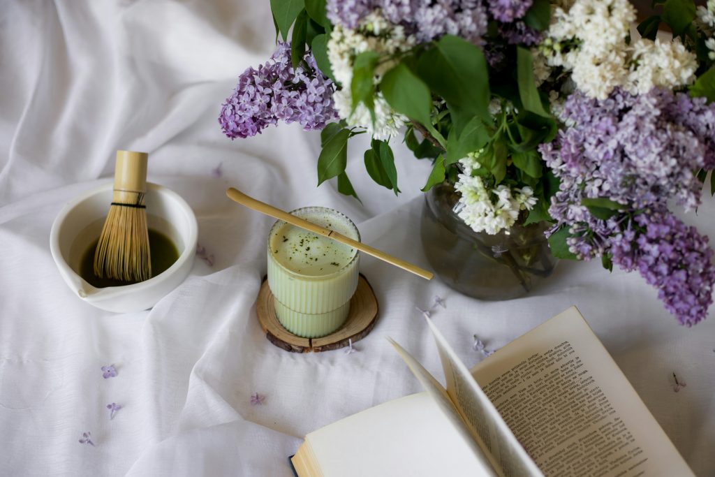 A matcha tea ritual scene with a bamboo whisk, fresh lilacs, and an open book, representing the Creative Vitality category