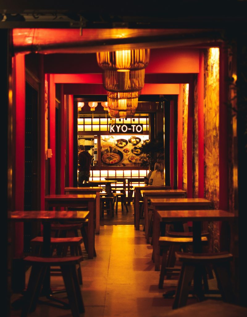 A warmly lit restaurant interior with red beams resembling a torii gate and hanging lanterns, evoking the Japanese mythological roots of Enso