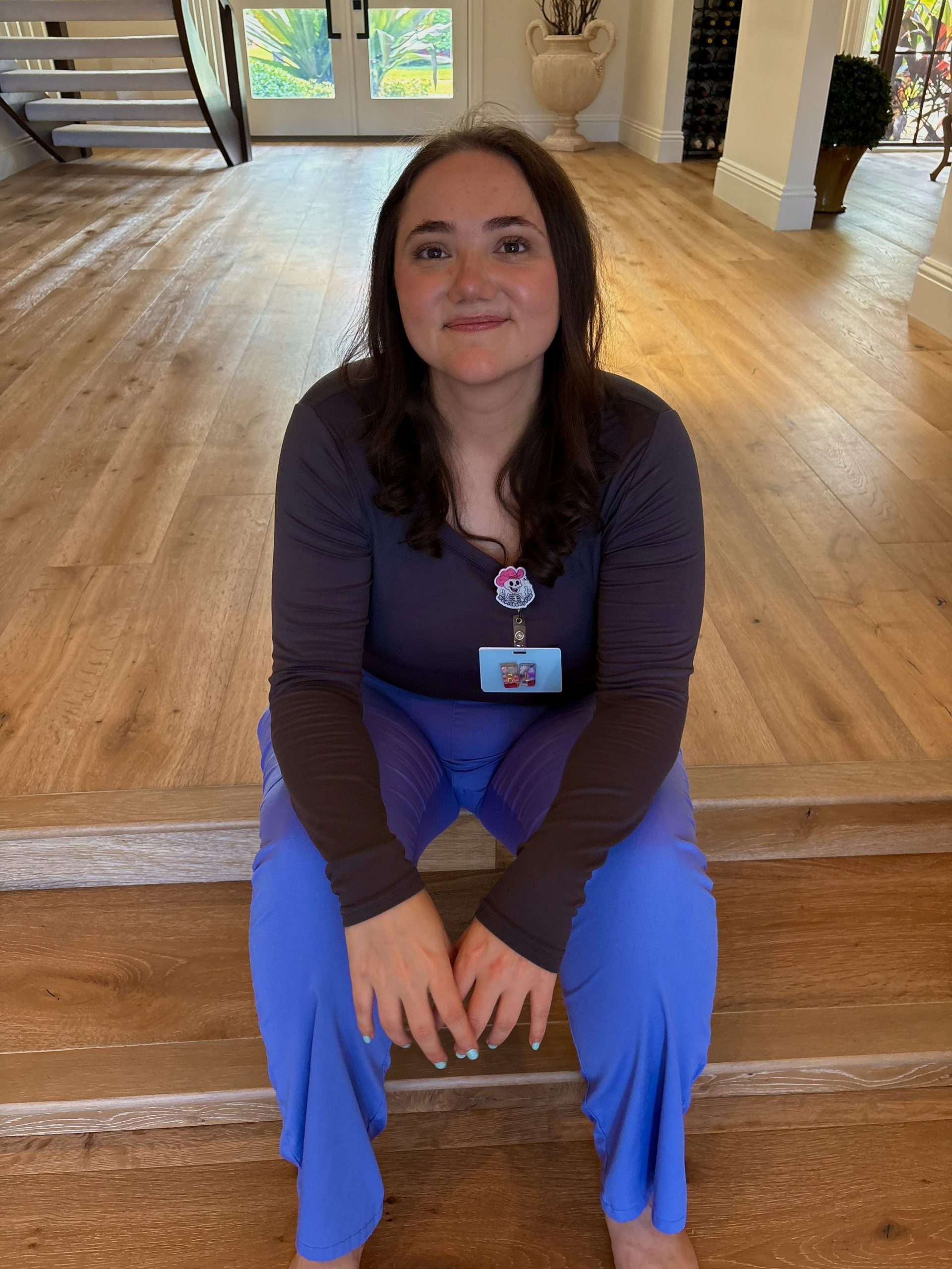 Lauren in blue scrubs and a dark top sitting on stairs with a badge
