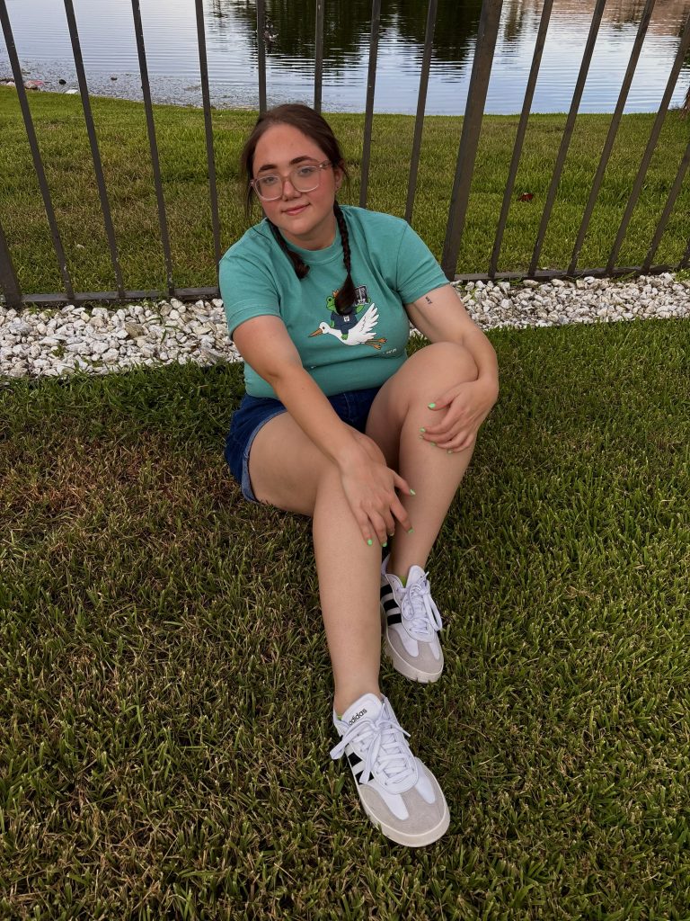 Radiology student sitting outdoors by a lake, wearing a teal "we x-ray at dawn" t-shirt.